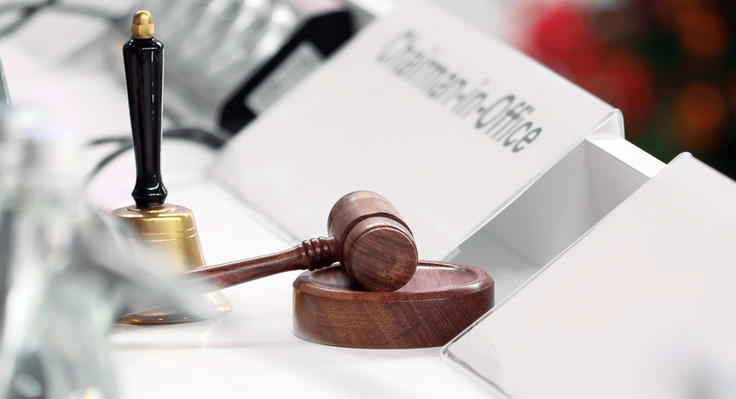 A bell, a gavel and a sign reading Chairman-in-Office on a white conference table.