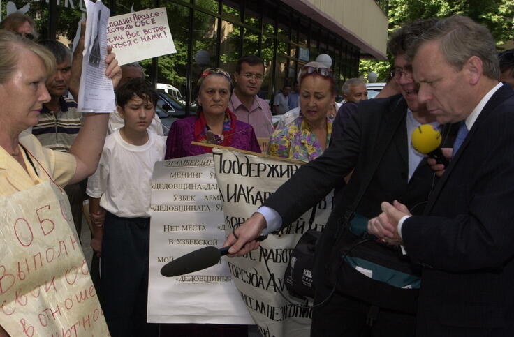 The Netherlands foreign minister in 2003, Jaap de Hoop Scheffer, looks at posters held up by protesters while a journalist with a microphone in his hand points at the posters to translate their meaning.