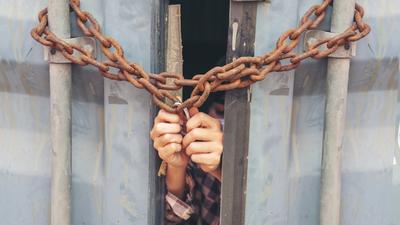 Hands gripping iron bars through a chained and locked gate.