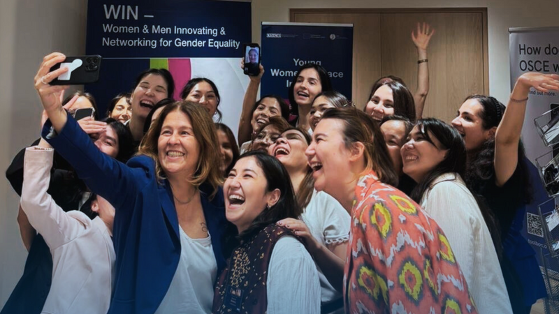 Group of women smiling and taking a selfie in an indoor setting, looking cheerful and engaged.