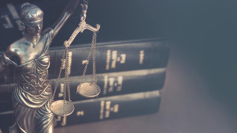 Lady Justice statue beside a stack of law books, in soft focus.