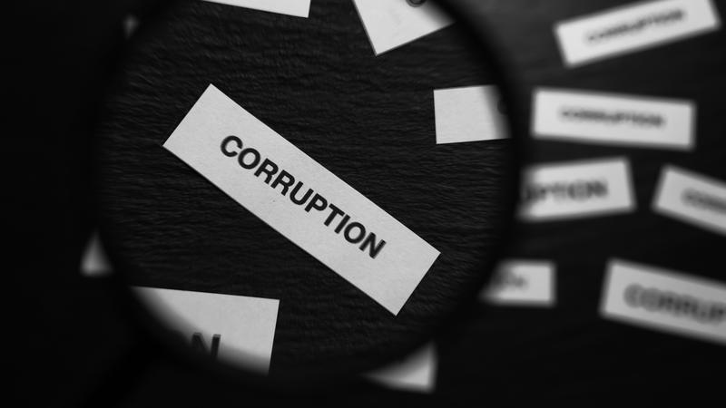 Magnifying glass highlighting the word "corruption" on a black background.