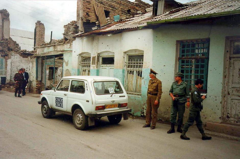 OSCE vehicle and military personnel next to damaged buildings.