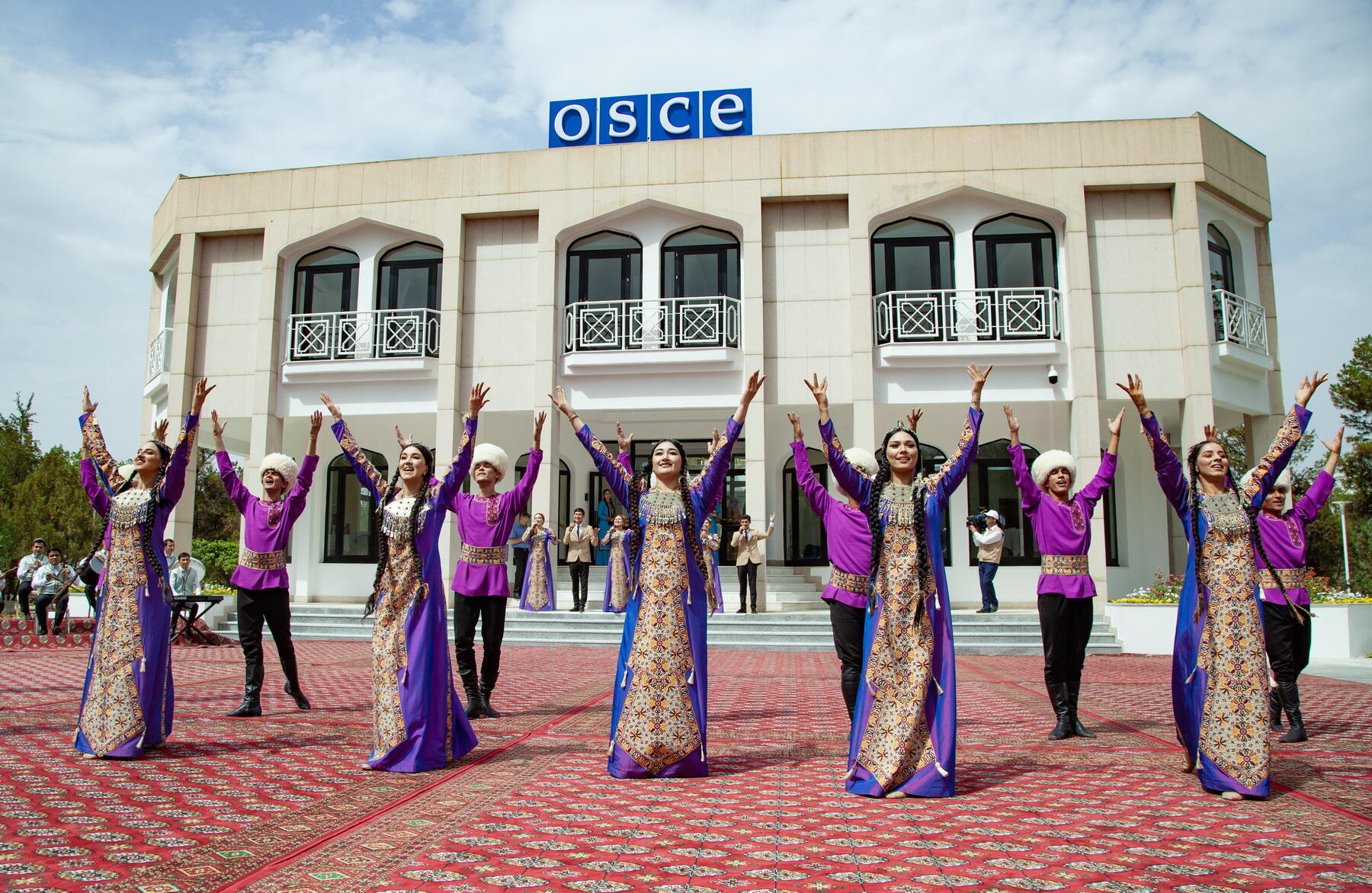 Traditional dancers in colorful attire performing in front of an OSCE building.