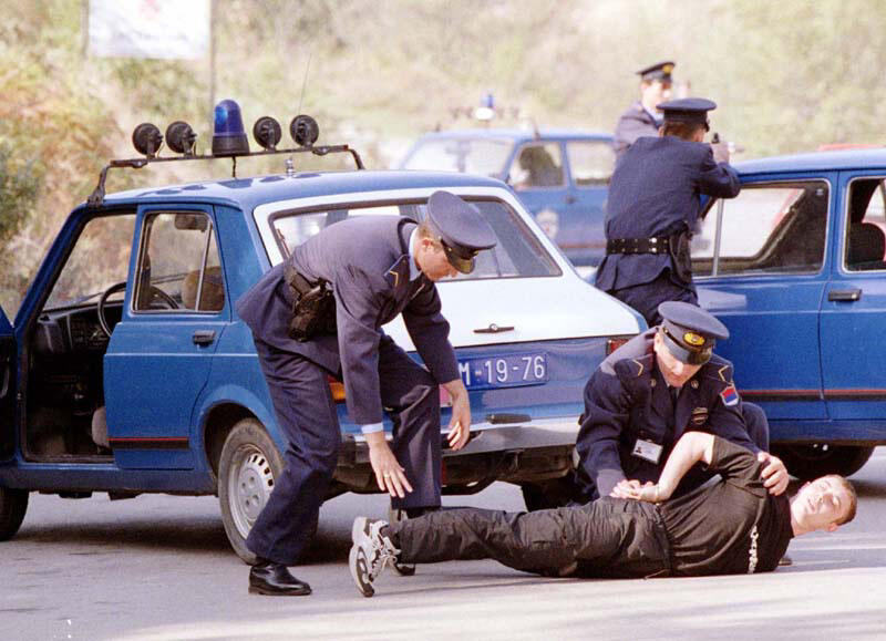 Police officers detaining a person on the ground next to blue police cars.